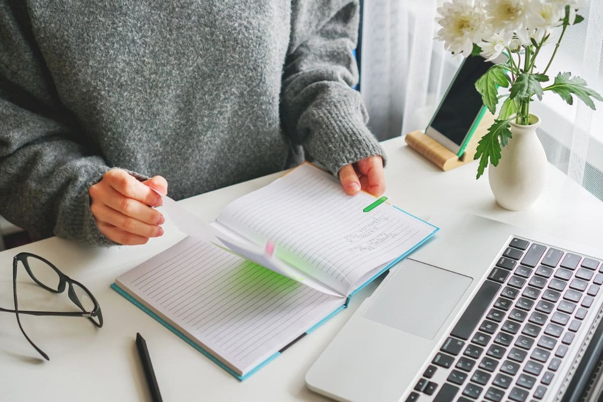 A woman working from her home office at a desk and flipping through a planner.