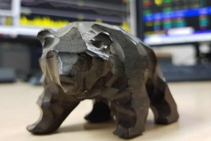 Tabletop model of a bear sat on desk in front of monitors showing stock charts